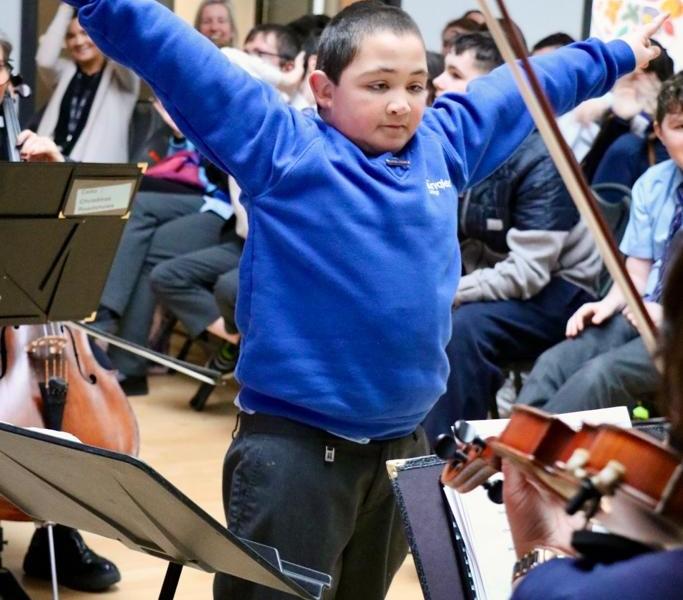 Pupil conducting staff orchestra during roadshow performance
