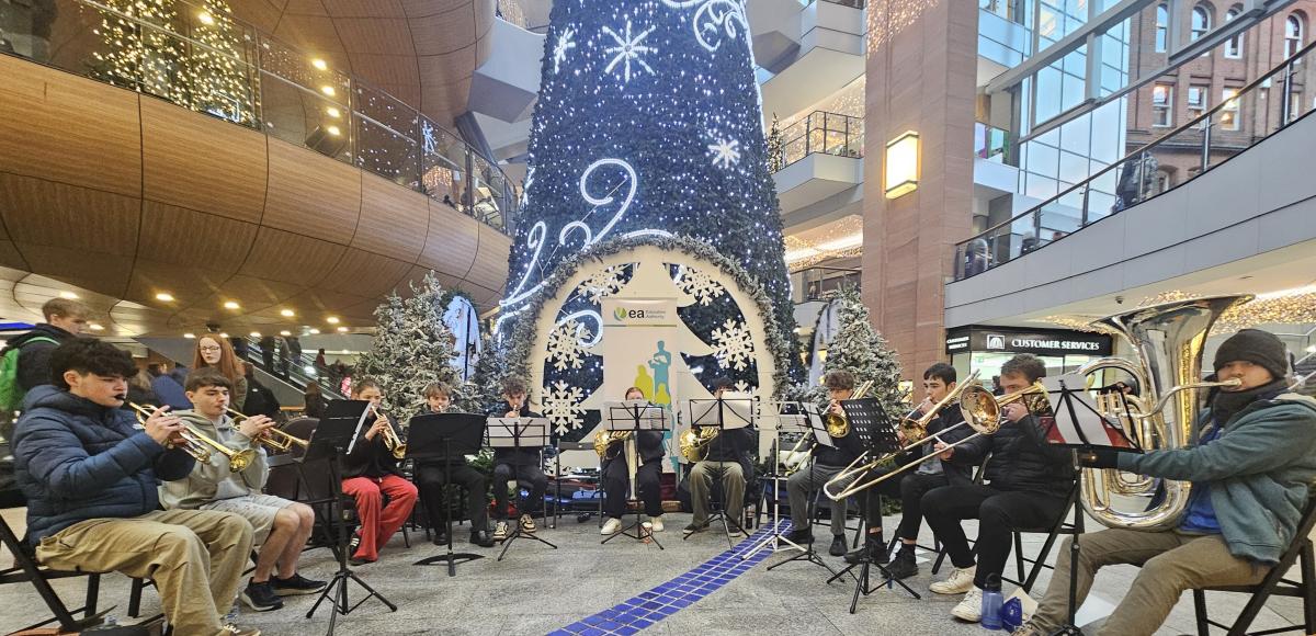 Children and young musicians playing brass instruments in front of a Christmas tree.