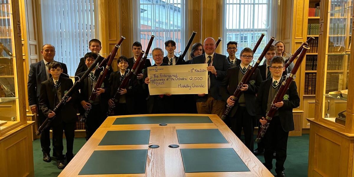 Children and young people holding bassoons, receiving a large cheque donation.