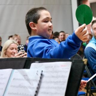 pupil with paddles conducting staff orchestra during roadshow performance