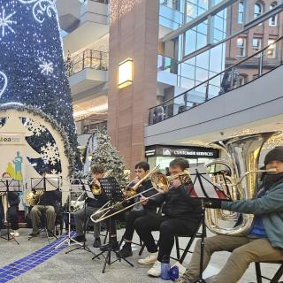Children and young musicians playing brass instruments in front of a Christmas tree.