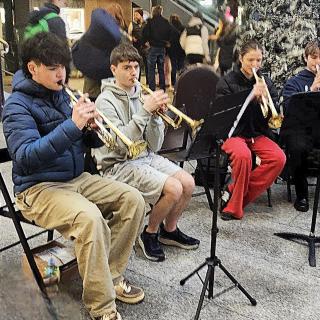 Young people playing trumpets, sitting in front of Christmas decorations.