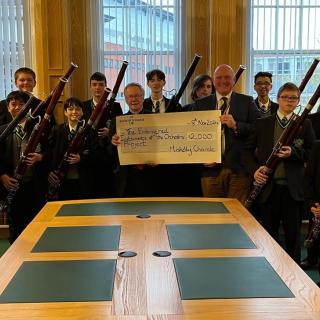 Children and young people holding bassoons, receiving a large cheque donation.