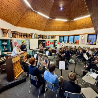 Phil Coulter speaking to students who are sitting with their instruments  in a hall