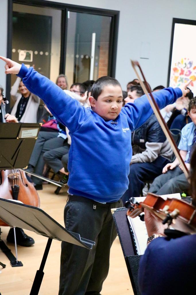 Pupil conducting staff orchestra during roadshow performance